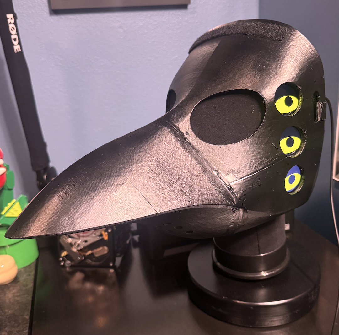 The finished product, powered on. In this photo, the mask is attached to a stand I built in early 2026, which consists of a mannequin head that&rsquo;s mounted to a 5 pound weight wrapped in wood. The electronics are being powered externally here for convenience; when the costume was being worn, everything was powered by a battery inside the beak.